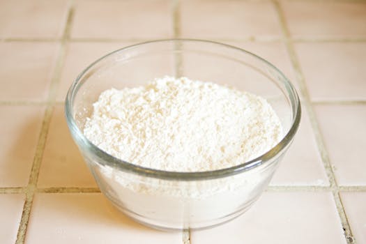 Close-up of a clear glass bowl containing flour on a tiled kitchen counter.