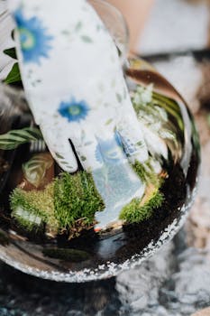 Close-up of a floral gardening glove arranging moss and plants in a glass terrarium.
