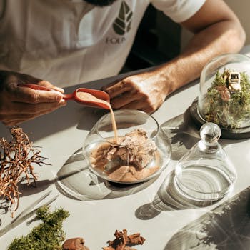 Close-up of a person creating a terrarium with sand, moss, and glass containers.